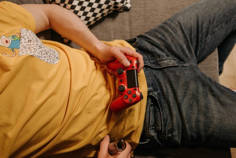 Person holding a red game controller while relaxing on a couch in comfortable clothes.